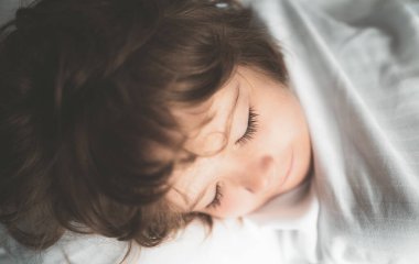 Beyaz çarşaflarla rahat bir yatakta uyuyan çocuklar..