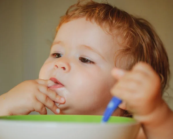 Lick tasty fingers. Portrait of cute Caucasian child kid with spoon. Hungry messy baby with plate after eating puree. — Stock Photo, Image