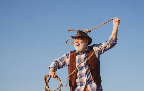 Vaquero occidental mayor lanzando soga de lazo. Barbudo hombre del oeste salvaje con chaqueta marrón y sombrero de captura de caballo o vaca. Rodeo o rancho. — Foto de Stock