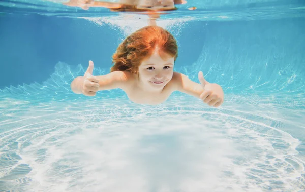 O miúdo nada debaixo de água na piscina. Menino nadando debaixo de água com os polegares para cima. — Fotografia de Stock