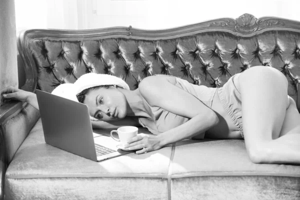 Bella giovane donna sensuale con computer portatile e caffè in pigiama godendo il tempo libero del mattino in camera da letto a casa. — Foto Stock