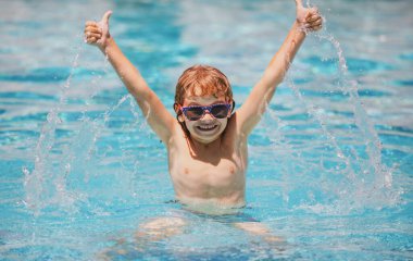 Parmağını kaldırmış yüzme havuzunda yüzen çocuk. Suyun içine su sıçratır, boş zamanlarında kollarını açarsın..
