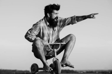 Küçük bir bisiklet süren çılgın bir adam. Heyecanlı genç erkek küçük bir bisiklet sürüyor ve mutluluğu işaret ediyor. Üç tekerlekli bisiklete binen genç adam.