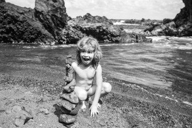 Heyecanlı çocuk çakıl taşı plajında taş piramit yapıyor. Dengeyi, zen, ahengi, dengeyi simgeliyor..