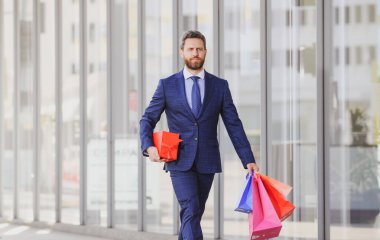 Alışveriş torbaları taşıyan, şehirde yürüyen bir iş adamı..