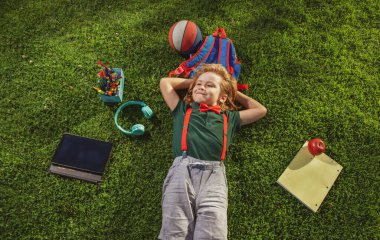 Doğadaki okul çocuğu. Okul malzemesi taşıyan inek öğrenci. Çocuk çimlerin üzerinde yatıyor. Rüyamda ders çalışıyordum. Yeşil çimlerin üzerinde uzanan küçük bir çocuk manzarası.