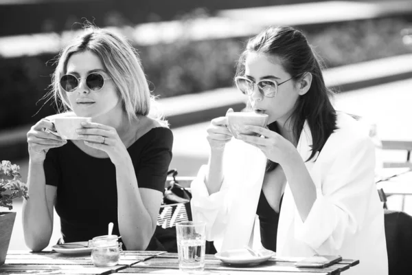Dos hermosas chicas con tazas de café en la cafetería de verano. Amigos en la cafetería al aire libre. Retrato al aire libre de dos jóvenes hermosas amigas tomando café. —  Fotos de Stock