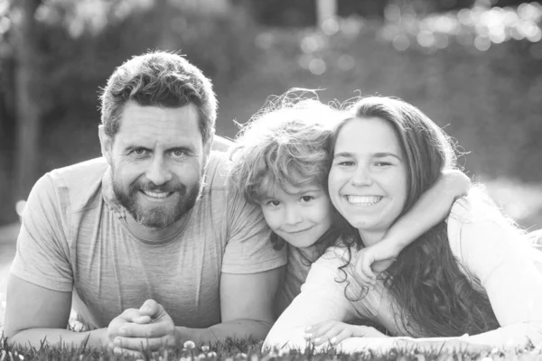 Nettes Familienporträt, das sich umarmt und umarmt. Familie liegt auf Gras im Park. Eltern und Kinder im Urlaub spielen gemeinsam im Freien. — Stockfoto