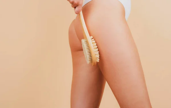 Woman makes massage with a wooden soft massage brush for body. Woman legs and buttocks ass without cellulite. Skin treatment. Anti-cellulite body massage for leg and butt. Spa and wellness. — Photo