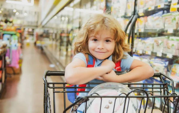 Söt pojke på mataffär eller stormarknad med varor i kundvagn. — Stockfoto