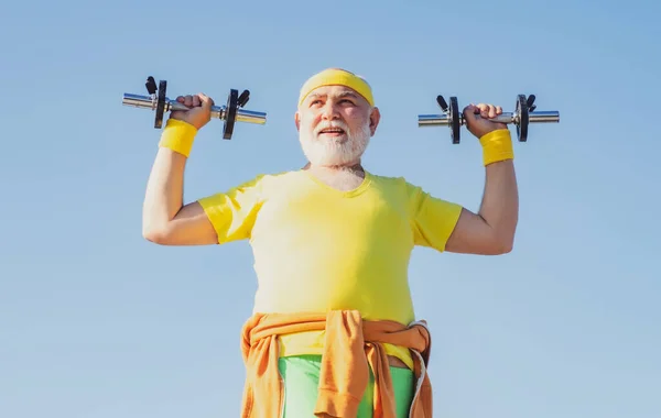 Vecchio sportivo che esercita con sollevamento manubri su sfondo cielo blu. Isolato, ricevi lo spazio. Buon uomo anziano che si allena con il sollevamento di manubri all'aperto. Stile di vita sano concetto. — Foto Stock