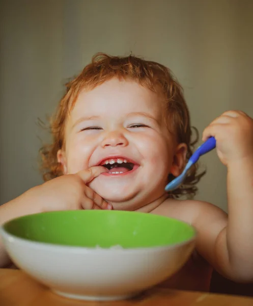 Happy launching baby eating himself with a spoon. Lick tasty fingers. — Stock Photo, Image
