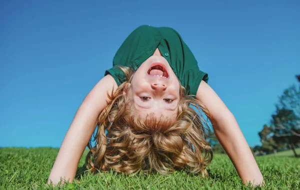 Ritratto di un bambino felice sorridente a testa in giù sul prato. Ragazzina che ride. Espressive espressioni facciali. Sport all'aria aperta sano attivo. Attività divertenti. — Foto Stock