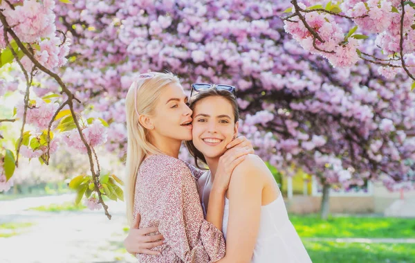 Chicas de primavera en flores. Retrato al aire libre de joven hermosa feliz sonriente pareja femenina posando cerca del árbol floreciente. — Foto de Stock