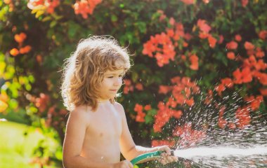 Çocuk bahçede oynuyor, hortumdan dökülüyor, yağmur yağıyor. Mutlu çocukluk kavramı. Çocuk ağaçlara su döküyor. Arka bahçedeki bitkilerle ilgilenen çocuk..