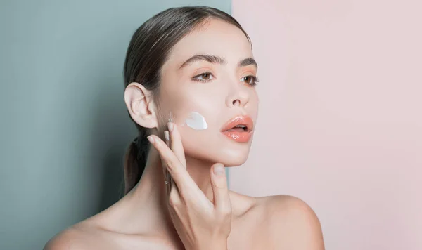 Menina atraente colocando creme anti-envelhecimento em seu rosto. Retrato de close-up da menina com pele lisa saudável . — Fotografia de Stock