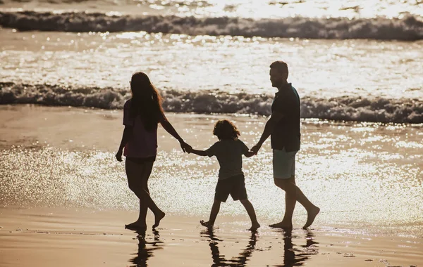 Silhouet van vader, moeder en kind zoon hand in hand en lopend op het strand. — Stockfoto