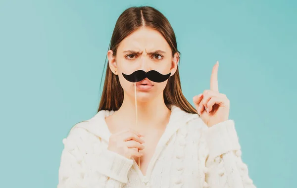 Woman with fake mustache having fun. Funny female actress with finger up isolated on blue background.