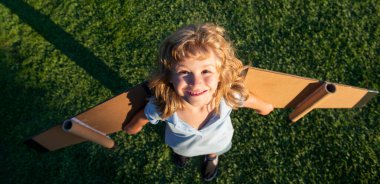Parktaki yeşil çimlerde oyuncak uçak kanatlarıyla oynayan çocuk. Bir pilot olmayı hayal et. Süper kahraman uçuyor..