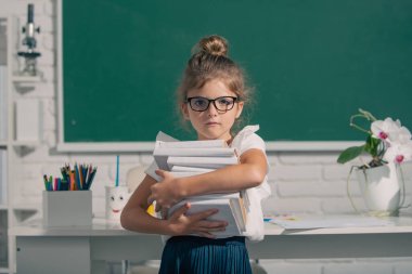 Kara tahtada kitapları olan gözlüklü inek öğrenci. Küçük kız okulda ders alıyor. Sınıfta ilkokul çocuğu.