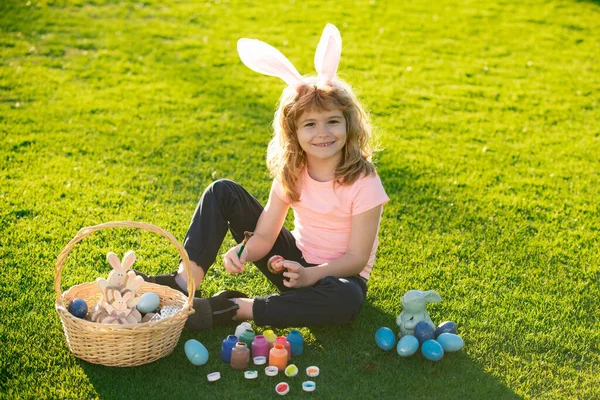 Pasen kinderen jongen in konijnenoren jagen paaseieren buiten. Schattig kind in konijnenkostuum met konijnenoren die plezier hebben in het park. Grappige jongen, paashaas kinderen. — Stockfoto