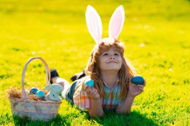 Tavşan kulaklı çocuk dışarıda paskalya yumurtası avlıyor. Paskalya kutlaması yapan, çimlere uzanan bir çocuk. Paskalya yumurtası avı.