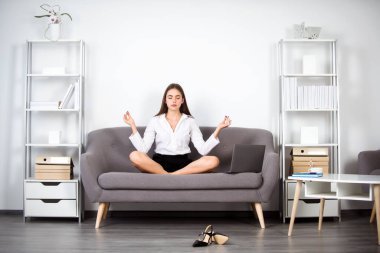 Genç meditasyon işkadını, sekreter kız modern bir ofiste işyerindeki kanepede yoga egzersizi yapıyor. Çalışanlar denge uyumunu hisseder..