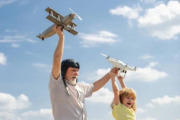 青空と雲の背景の上に飛行機とクワッドコプターのドローンを持つ祖父と息子。男は祖父と孫を生み出す。子供との高齢者の親戚. — ストック写真