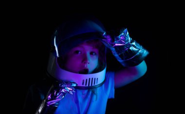 Miğferli ve koruyucu uzay giysili küçük astronot portresi. Heyecanlı çocukların yüzlerini neon rengine yakın tut.