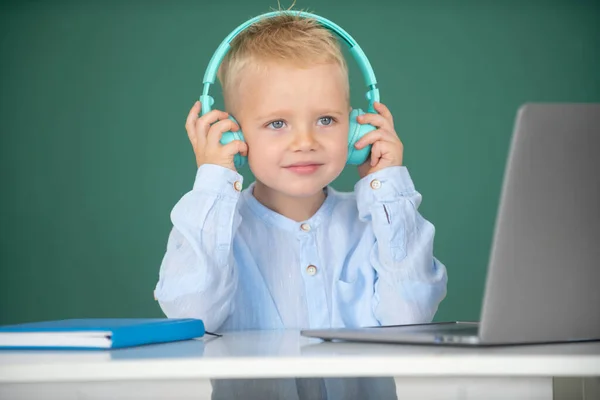 Roztomilý chlapec ve sluchátkách, studuje s laptopem ve třídě, poslouchá audio lekce. Školení počítače. — Stock fotografie