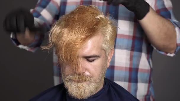 Kadeřník česá mužské vlasy. Proces chlapa, co má vlasy obarvené v kadeřnickém salónu. Barevné blond vlasy pro vousatý hipster chlap. — Stock video