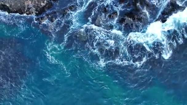 Barevné vody oceánu, víří kolem skalnatého a malebného pobřeží. Mořské vlny se lámou přes kameny. — Stock video