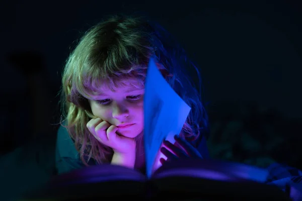 Barn läser en bok i sängen innan de somnar. En liten pojke som ligger på sängen och läser böcker hemma. Lycklig barndom, drömmande barn. — Stockfoto
