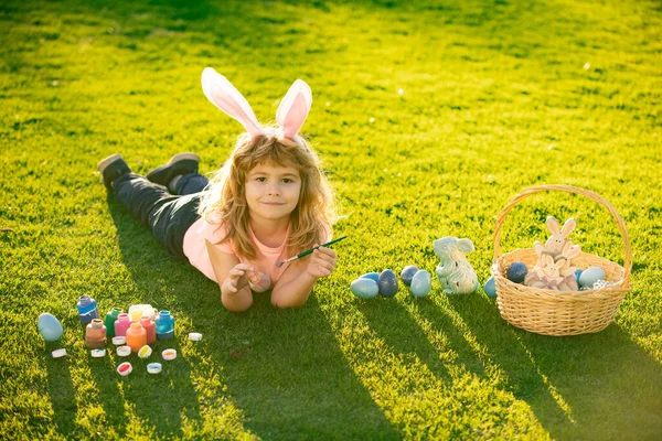 Jongetje met paaseieren en konijnenoren op gras. Pasen kinderen met konijnenoren en op gras achtergrond. — Stockfoto