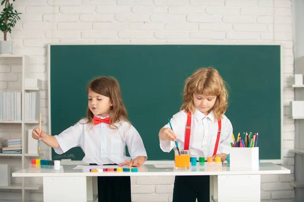 Niños de la escuela niña y niño pintando con pinturas de color y pincel en el aula. Lindos niños dibujan con lápices de colores. — Foto de Stock