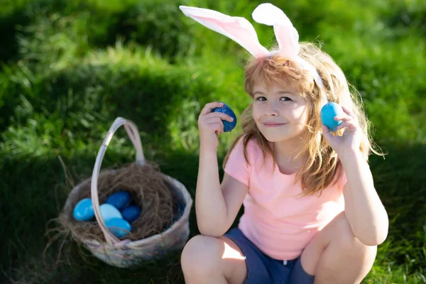 Paaseieren zoeken. Gelukkig Pasen voor kinderen. Jongen in konijnenoren met kleurrijke eieren spelen en jagen op paaseieren buiten. — Stockfoto