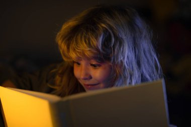 Çocuk uyumadan önce yatakta kitap okuyor. Evdeki küçük çocuk yatakta uzanıp kitap okuyor. Çocuğun gelişimi. Akıllı çocuk..