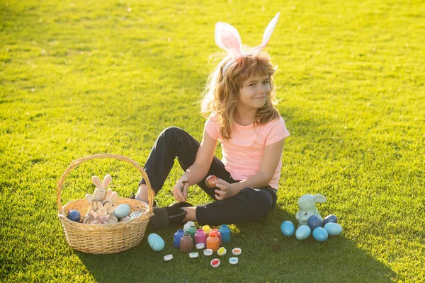 Paashaas kinderen. Kleine jongen in konijnenoren die eieren schildert. Schattig jongetje, paashaas kinderen lente outdoor. — Stockfoto
