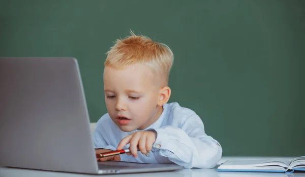 Školní dítě používá digitální PC notebook ve třídě. Portrét legračního žáka programu základní školy. Vtipné blondýny žák na tabuli. — Stock fotografie