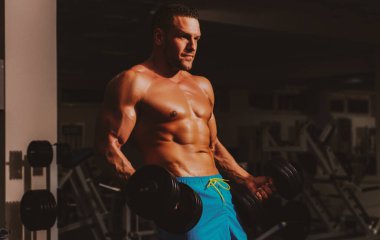 Dambıl egzersizi yapıyor. Spor salonunda vücut geliştirici. Antrenman ve idman. Çıplak gövdeli bir sporcu. Sportif egzersiz..
