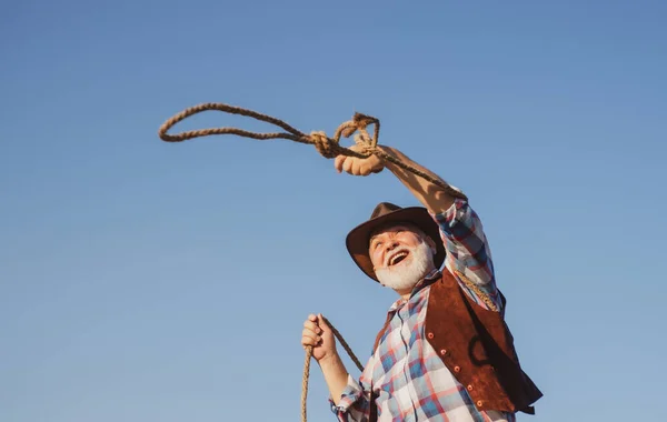 Old western cowboy with lasso rope. Bearded wild west man with brown jacket and hat. — Stock Photo, Image