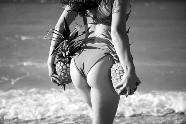 Frauengesäß mit Ananas im Badeanzug-Bikini auf Sandmeer. — Stockfoto