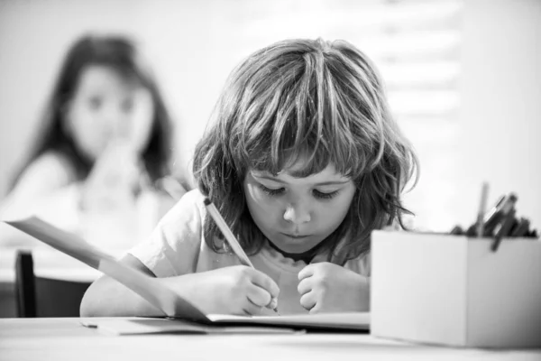 Діти в школі. Шкільна дитина щось пише в книжці і сидить за столом у класі . — стокове фото