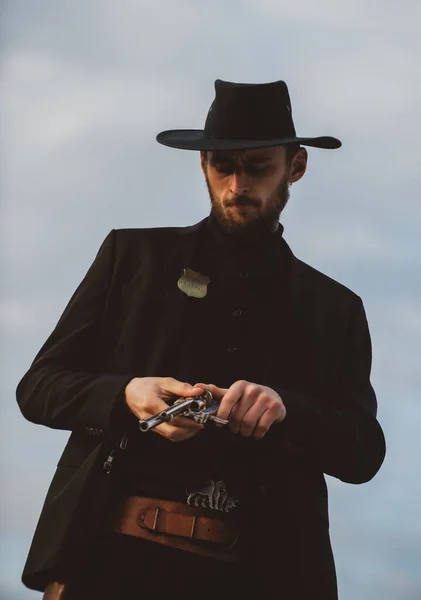 Tirador de vaquero en traje negro y sombrero de vaquero. Un hombre serio con armas del salvaje oeste, revólver retro y munición de mariscal. Sheriff occidental americano. Wild West quería concepto. —  Fotos de Stock