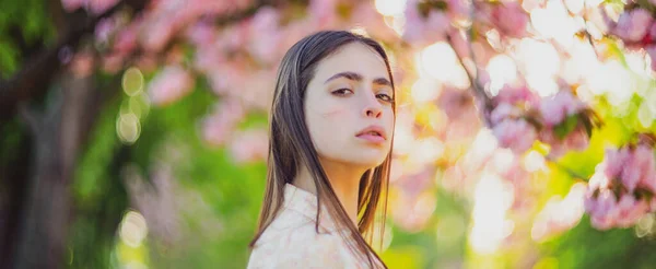 桜の木を背景にポーズをとる美しいロマンチックな若い女性。春と夏のインスピレーション。バナー春のデザイン、ウェブサイトのヘッダーの広告。春の花の背景. — ストック写真
