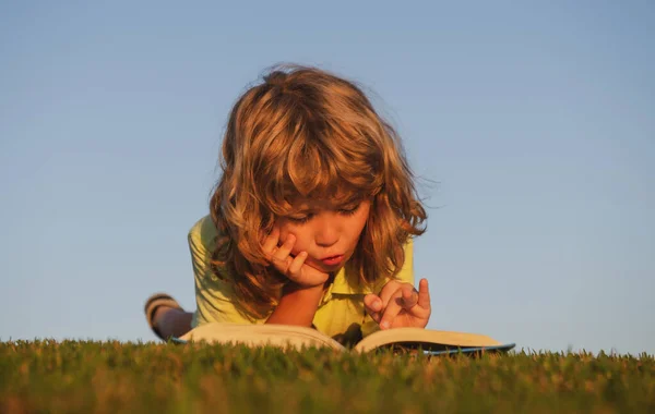 Smart pojke läser bok i parken utomhus. Smarta barn utomhus. — Stockfoto