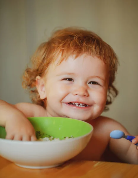 Het lanceren van het kind eet. Gelukkige baby eet zichzelf op met een lepel. Lachende baby die eten eet. Gezonde voeding voor kinderen. — Stockfoto