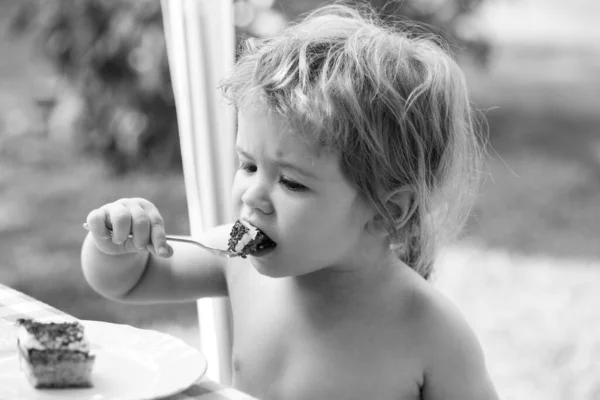 Bebé a comer bolo. Engraçado menino bonito comer bolo doce. Criança comendo sobremesa com colher no parque em piquenique. — Fotografia de Stock