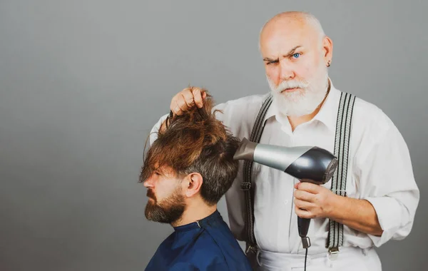 Sakallı adam berber dükkanında saç kurutma makinesiyle kuaför tarafından tımar ediliyor. Elinde saç kurutma makinesi tutan ciddi bir kuaför.. — Stok fotoğraf