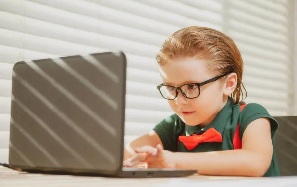Kleuterschooljongen doet haar huiswerk met laptop thuis. Online onderwijs concept, thuis schoolgaande leerling. — Stockfoto